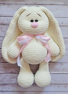 a white stuffed animal with a pink ribbon around its neck sitting on a wooden surface