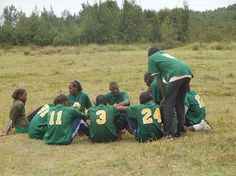 a group of young people sitting on top of a grass covered field next to each other