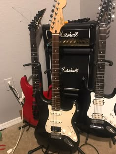 three electric guitars sitting next to each other on the floor in front of a wall