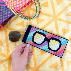 a hand is holding a small cross - stitch purse with sunglasses on it, next to a pair of sunglasses