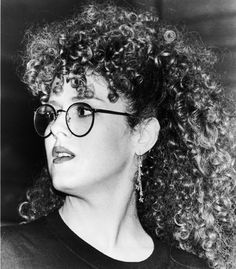 a black and white photo of a woman with curly hair wearing glasses looking off to the side