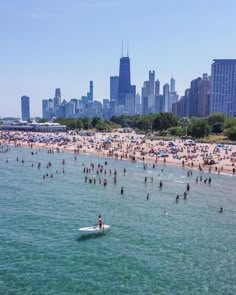 many people are on the beach and in the water, with skyscrapers in the background