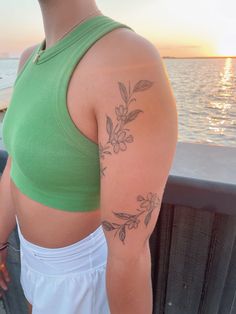 a woman with a flower tattoo on her left arm, standing next to the water