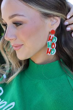 a woman wearing a green sweater and red earrings with the word ho hoo on it