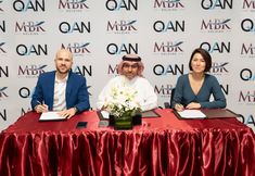 three people sitting at a table signing papers in front of a wall with red curtains