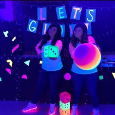 two young women standing in front of a neon sign with dices on the floor