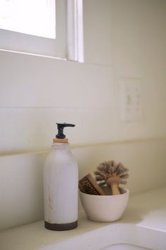 a white bathroom sink with a soap dispenser and brush in front of it