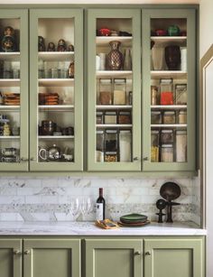 a kitchen with green cabinets and white marble counter tops in front of the cupboards