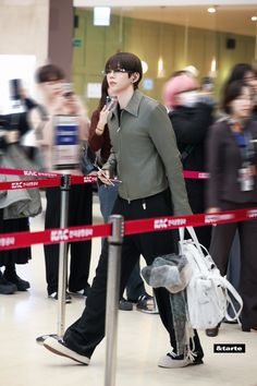 a woman walking through an airport with her hand in her pocket and other people behind her