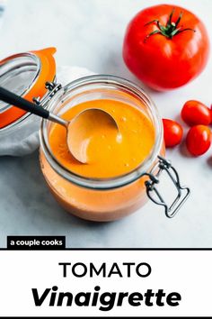 tomato sauce in a glass jar with a spoon and tomatoes around it on a white surface