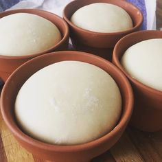 four brown bowls filled with dough on top of a wooden table