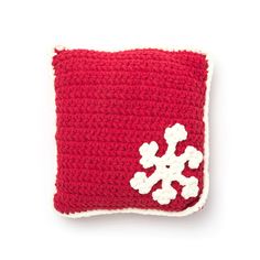 a red and white crocheted pillow with snowflakes on the front, sitting on a white surface