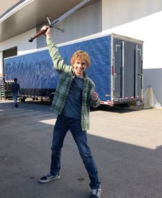 a young man holding up a baseball bat in front of a blue and white trailer