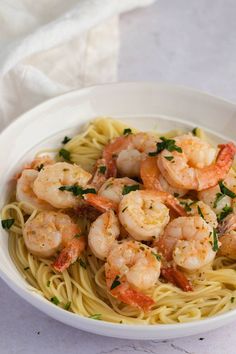 a white bowl filled with pasta and shrimp on top of a table next to a fork