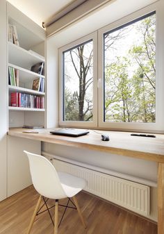 a white chair sitting in front of a window next to a wooden desk and bookshelf