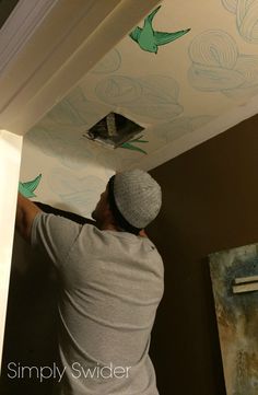 a man painting the ceiling with green birds on it