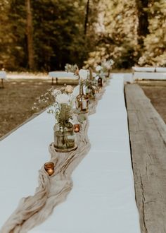 a long table with vases and candles on it in the middle of a forest