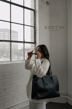 a woman holding a black handbag while standing next to a window