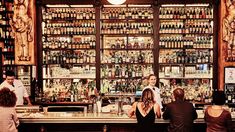 people are standing at the bar in front of shelves full of liquors and bottles