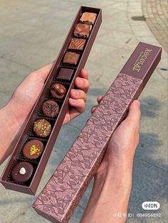 a person holding a box of chocolates in their hands on the ground with one hand