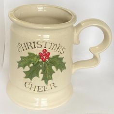 a white ceramic mug with holly leaves and red berries on the front, says christmas cheer