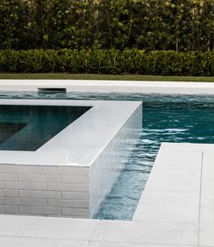 an empty swimming pool surrounded by hedges and trees in the backround, with water running through it