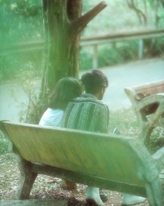 two people sitting on a bench in the park