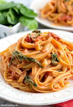 pasta with spinach and tomato sauce on a white plate next to basil leaves in the background