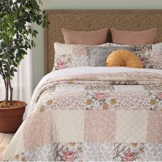 a bed with a flowered comforter and pillows on it in a room next to a potted plant