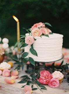 a white wedding cake with pink flowers and greenery on the top is surrounded by candles