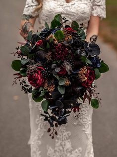 a woman in a white dress holding a bridal bouquet with red and black flowers