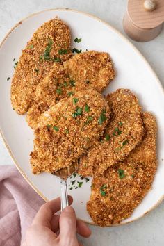 someone is holding a spoon over some fried chicken on a white plate with parsley