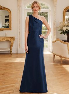 a woman standing in a room wearing a blue dress with one shoulder and an asymmetrical neckline