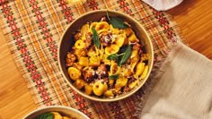 two bowls filled with pasta and vegetables on top of a wooden table next to a towel