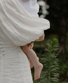 a woman in a white dress holding a baby wrapped in a shawl over her head