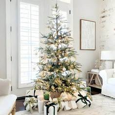 a decorated christmas tree in the corner of a living room with white walls and windows