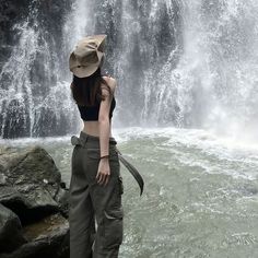 a woman standing in front of a waterfall with her back to the camera and wearing a hat