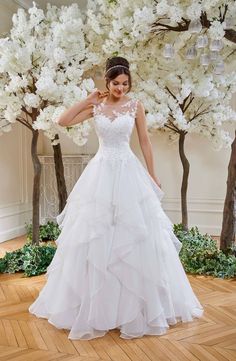 a woman in a white wedding dress standing next to some trees with flowers on it