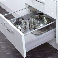 two pots and pans are in the bottom drawer of a kitchen cabinet that is open