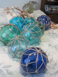 blue and green glass balls on a bed with rope wrapped around the edges, sitting on top of each other