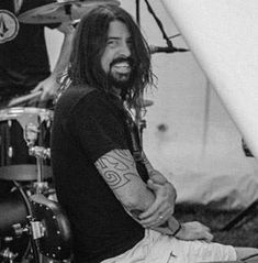 a man with long hair sitting on the ground next to a drum set and microphone