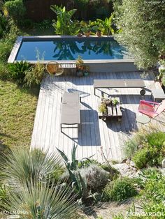 an aerial view of a backyard with a pool and decking area, surrounded by greenery