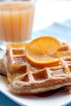 two waffles on a white plate with orange slices and juice in the background