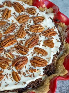 a pie topped with whipped cream and pecans in a red dish on a table