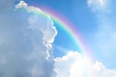 a rainbow in the sky with clouds and blue sky behind it on a sunny day