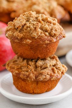 two muffins stacked on top of each other on a plate next to an apple