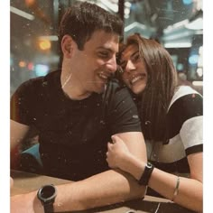 a man and woman sitting next to each other in front of a table with a cell phone