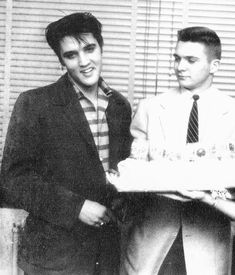 two men holding a cake with candles on it in front of a window and shutters