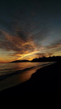 the sun is setting over the ocean with clouds in the sky and water on the beach