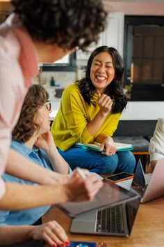 three women sitting on the floor laughing and looking at a laptop computer while another woman sits in front of them